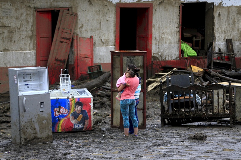 A woman with her baby stands in front of a damaged house after a landslide sent mud and water crashing onto homes close to the municipality of Salgar in Antioquia department, Colombia May 19, 2015. A landslide sent mud and water crashing onto homes in a town in Colombia's northwest mountains on Monday, killing more than 50 people and injuring dozens, officials said.REUTERS/Jose Miguel Gomez