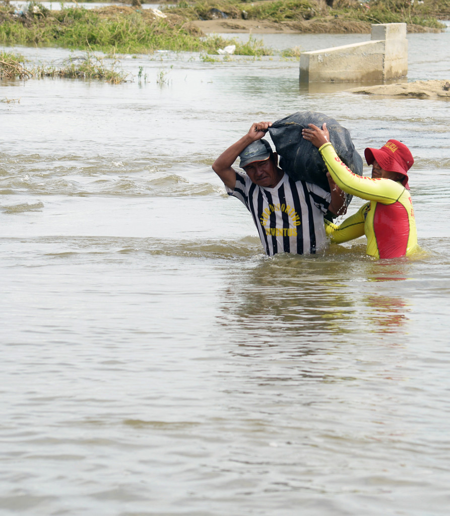 Local residents cross swollen flooded streams to recover their belongings from their homes in small villages close to the city of Piura, in northern Peru, on March 31, 2017.  Thousands have been forced to abandon their homes in Peru after unusually heavy seasonal rains caused rivers and streams to overflow their banks, flooding cities and fields. / AFP PHOTO / MIGUEL ARREATEGUI