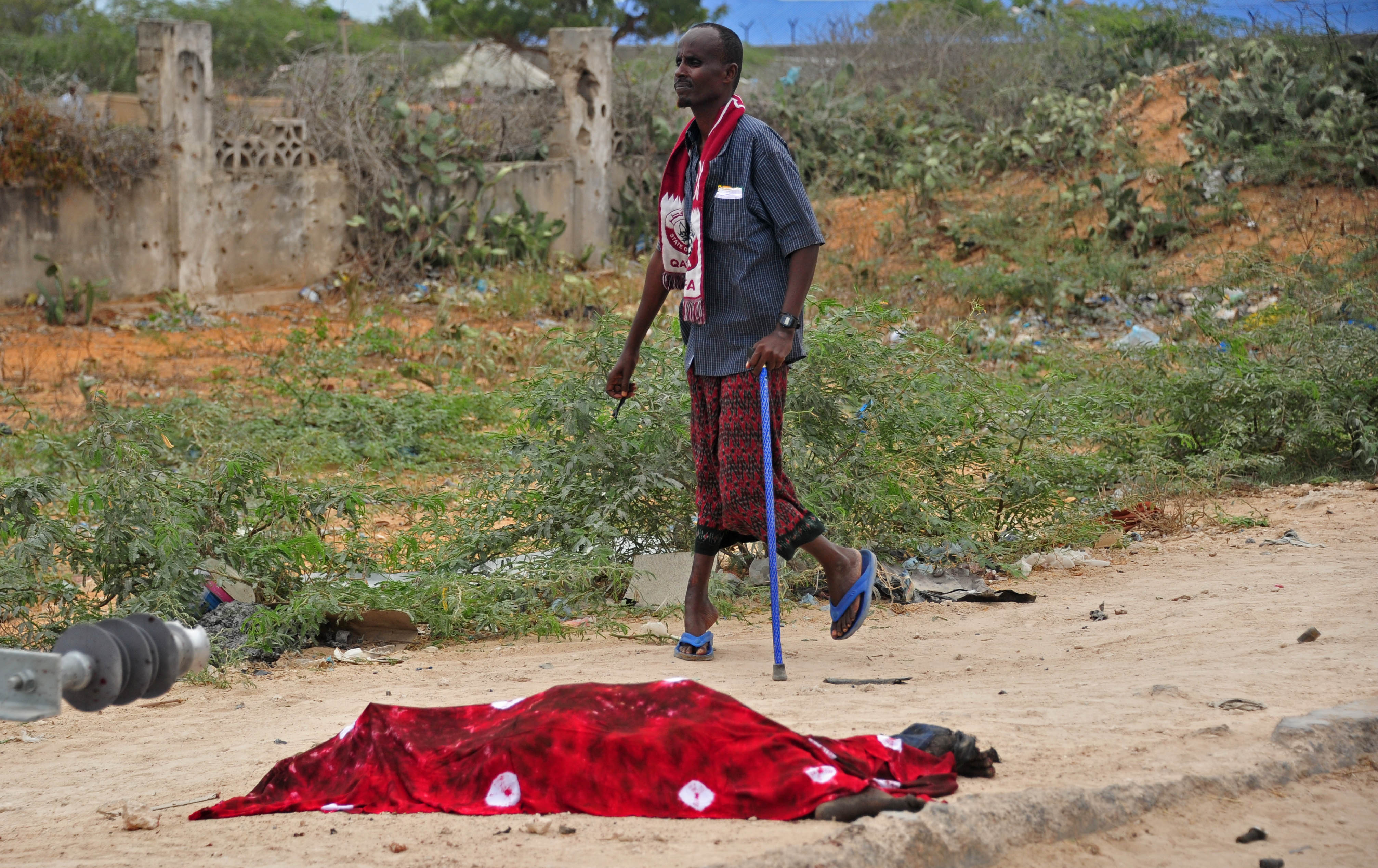A man walks past a covered dead body after a suicide car attack near the Defense Ministry in Mogadishu on April 9, 2017. A car bomb attack targeting Somalia's new army chief on April 9, 2017, killed at least five people, including four civilians and a soldier, said an AFP reporter at the scene. The Mogadishu attack against the army convoy was claimed by the Shabaab extremist group and came only days after Mohamed Jama Irfid, who was not hurt, was appointed to head the country's army, a security source said.  / AFP PHOTO / Mohamed ABDIWAHAB