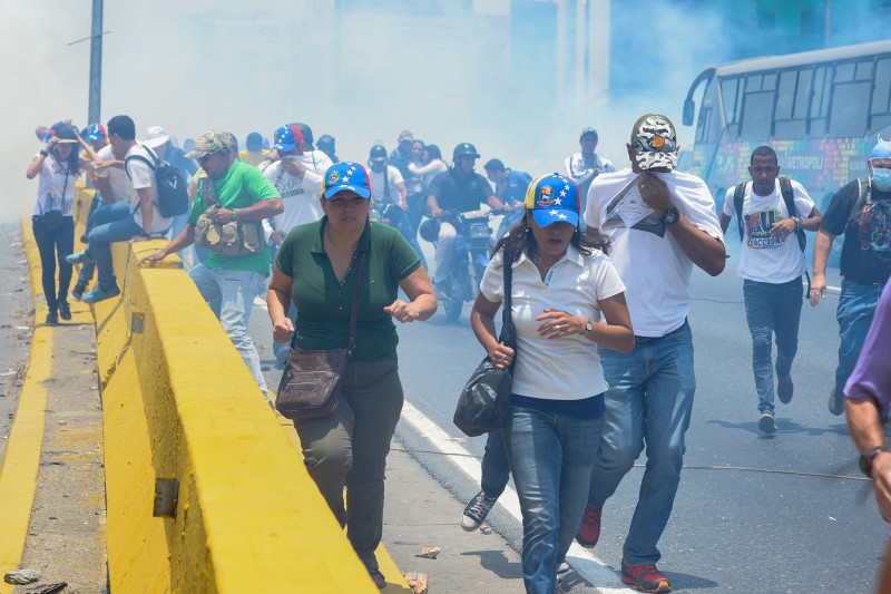 Opposition activists run away from tear gas fired by riot police during a protest against President Nicolas Maduro's government in Caracas on April 10, 2017. Venezuela's political crisis intensified last week when the Supreme Court issued rulings curbing the powers of the opposition-controlled legislature. The court reversed the rulings days later, but the opposition intensified its protests from that moment. / AFP PHOTO / FEDERICO PARRA