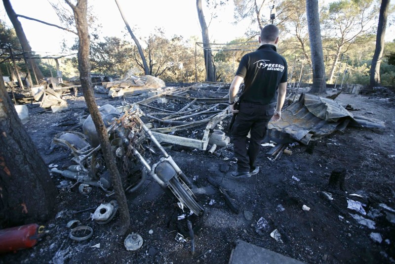 A security guard inspects the burnt remains of mobile homes in the camping Pin de la Legue, some 10 kilometers from Frejus, southern France, July 27, 2015. Fires broke out near Frejus and some 10,000 people in three campings areas were evacuated for their security according to local authorities.   REUTERS/Jean-Paul Pelissier