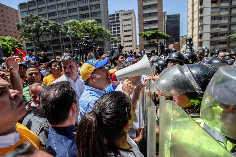 The President of the National Assembly Julio Borges using a megaphone addresses riot police agents during a protest against Nicolas Maduro's government in Caracas on April 4, 2017. Protesters clashed with police in Venezuela Tuesday as the opposition mobilized against moves to tighten President Nicolas Maduro's grip on power. Protesters hurled stones at riot police who fired tear gas as they blocked the demonstrators from advancing through central Caracas, where pro-government activists were also planning to march. / AFP PHOTO / JUAN BARRETO