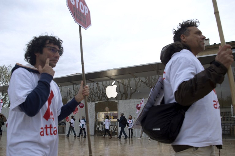 Activistas de la Asociación para la Tributación de Transacciones Financieras y Acción Ciudadana (ATTAC) tienen pancartas mientras otros pintan en blanco la fachada de una tienda de Apple durante una manifestación para denunciar evasión y opacidad el 1 de abril de 2017 en Aix-en-Provence, sur de Francia. AFP