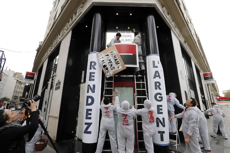 Un activista de la Asociación para la Tributación de las Transacciones Financieras y la Acción Ciudadana (ATTAC) tiene una pancarta que dice "multinacionales, paga tu parte", mientras otros activistas pintan en blanco las ventanillas de un banco de la Société Générale en la avenida de los Campos Elíseos. AFP PHOTO