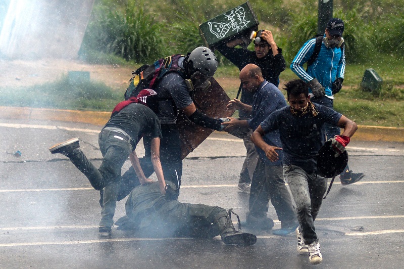 Opposition demonstrators kick a riot policeman during clashes in Caracas, on May 24, 2017. Venezuela's President Nicolas Maduro formally launched moves to rewrite the constitution on Tuesday, defying opponents who accuse him of clinging to power in a political crisis that has prompted deadly unrest. / AFP PHOTO / FEDERICO PARRA