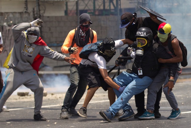 Demonstrators help a journalist who was injured in a leg while covering clashes between demonstrators and the  Bolivarian National Guard during a protest in Caracas, Venezuela, Monday, April 10, 2017. Opponents of President Nicolas Maduro protested on the streets of the capital as part of an ongoing protest movement that shows little sign of losing steam. (AP Photo/Ariana Cubillos)