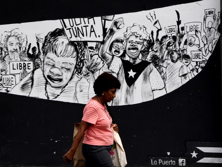 (FILES) This file photo taken on May 16, 2017 shows a Puerto Rican woman walking past protest murals on May 16, 2017 in San Juan, Puerto Rico, as the former Spanish colony of 3.5 million, now a US territory, struggles under a mountain of debt. The governor of Puerto Rico announced that the US territory would seek a form of bankruptcy protection to restructure its $70 billion debt, the largest municipal restructuring in US history. / AFP PHOTO / Mark RALSTON / With AFP Story by Elodie CUZIN: Puerto Rico's bankruptcy leaves US island facing hard times.