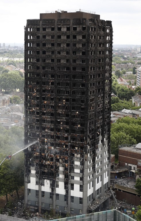 An automated hose sprays water onto Grenfell Tower, a residential tower block in west London that was caught in a huge blaze on June 14, 2017. Firefighters searched for bodies today in a London tower block gutted by a blaze that has already left 12 dead, as questions grew over whether a recent refurbishment contributed to the fire. / AFP PHOTO / Tolga AKMEN