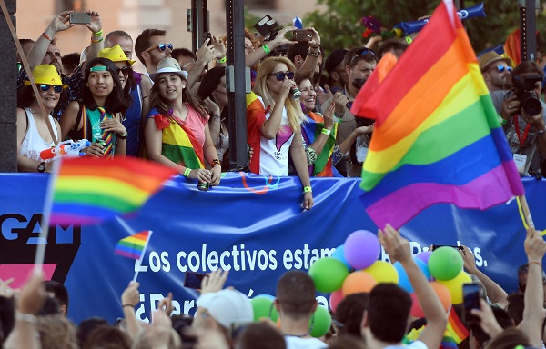 Spectators wave rainbow flags as participants ride on a float during the WorldPride 2017 parade in Madrid on July 1, 2017. Revellers took to the rainbow streets of Madrid today in the world's biggest march for gay, lesbian, bisexual and transgender rights. Carried along by the slogan "Viva la vida!" (Live life!), the parade of 52 floats started partying its way through the centre later afternoon in celebration of sexual diversity, under high security.  / AFP PHOTO / CURTO DE LA TORRE