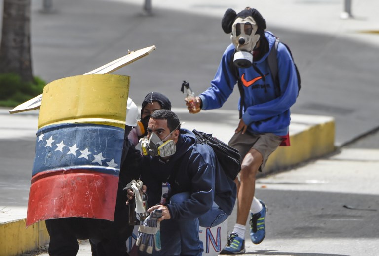 Venezuelan opposition activists remain behind a shield as they clash with riot police during a protest against Venezuelan President Nicolas Maduro in Caracas on July 10, 2017. Venezuela hit its 100th day of anti-government protests Sunday, amid uncertainty over whether the release from prison a day earlier of prominent political prisoner Leopoldo Lopez might open the way to negotiations to defuse the profound crisis gripping the country. / AFP PHOTO / JUAN BARRETO