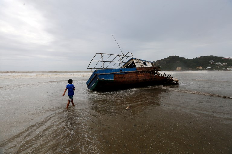 A boy walks towards a stranded boat in San Juan del Sur beach, following the passage of Tropical Storm Nate, in Rivas some 140km from Managua, Nicaragua, on October 6, 2017 Tropical Storm Nate gained strength as it headed toward popular Mexican beach resorts and ultimately the US Gulf coast after dumping heavy rains in Central America that left at least 22 people dead. / AFP PHOTO / INTI OCON