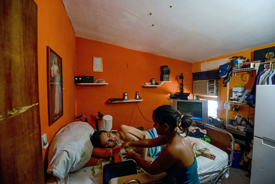 Daikellys Mosquera (R), 13, helps his quadriplegic dad Marco Guillen, to drink water at their house in Barquisimeto, Lara state, Venezuela on October 23, 2017. Marco Guillen became quadriplegic in an accident twelve years ago, amid Venezuela's deep economical crisis he desperately asks President Maduro's government to help him to live with dignity, meeting his medical necessities otherwise he pleads for euthanasia. / AFP PHOTO / FEDERICO PARRA / TO GO WITH AFP STORY by MARGIONI BERMUDEZ