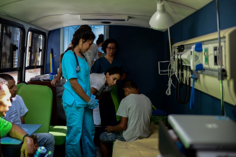 A volunteer talks to a homeless person after he is given a check-up on the PanaBus (FriendlyBus) in Caracas on November 27, 2017. Monday through Friday, the PanaBus (FriendlyBus) makes its way around the Venezuelan capital offering homeless people a shower, clean clothes, a meal, a health check-up and advice to help them out of their plight - a beacon of hope and solidarity in the midst of economic and political crisis and severe shortages of food and medicines. / AFP PHOTO / FEDERICO PARRA / TO GO WITH AFP STORY by MARGIONI BERMUDEZ