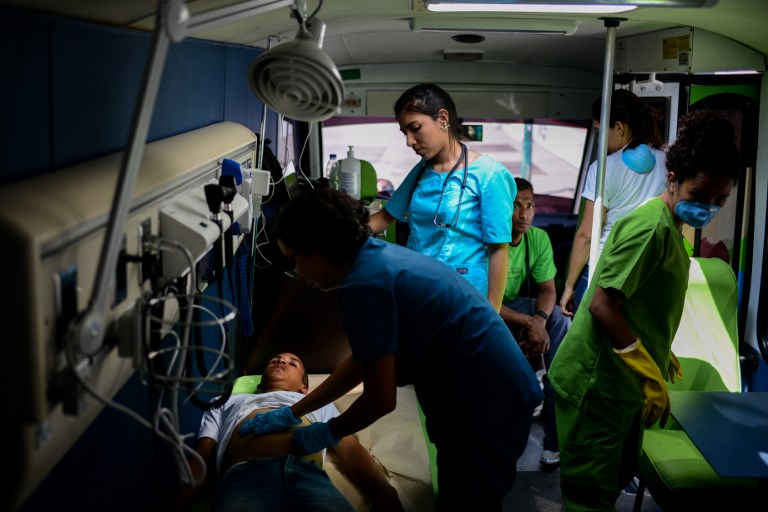 A volunteer doctor gives a homeless person a check-up on the PanaBus (FriendlyBus) in Caracas on November 27, 2017. Monday through Friday, the PanaBus (FriendlyBus) makes its way around the Venezuelan capital offering homeless people a shower, clean clothes, a meal, a health check-up and advice to help them out of their plight - a beacon of hope and solidarity in the midst of economic and political crisis and severe shortages of food and medicines. / AFP PHOTO / FEDERICO PARRA / TO GO WITH AFP STORY by MARGIONI BERMUDEZ