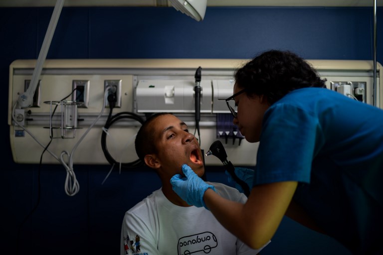 A volunteer doctor gives a homeless person a check-up on the PanaBus (FriendlyBus) in Caracas on November 27, 2017. Monday through Friday, the PanaBus (FriendlyBus) makes its way around the Venezuelan capital offering homeless people a shower, clean clothes, a meal, a health check-up and advice to help them out of their plight - a beacon of hope and solidarity in the midst of economic and political crisis and severe shortages of food and medicines. / AFP PHOTO / FEDERICO PARRA / TO GO WITH AFP STORY by MARGIONI BERMUDEZ